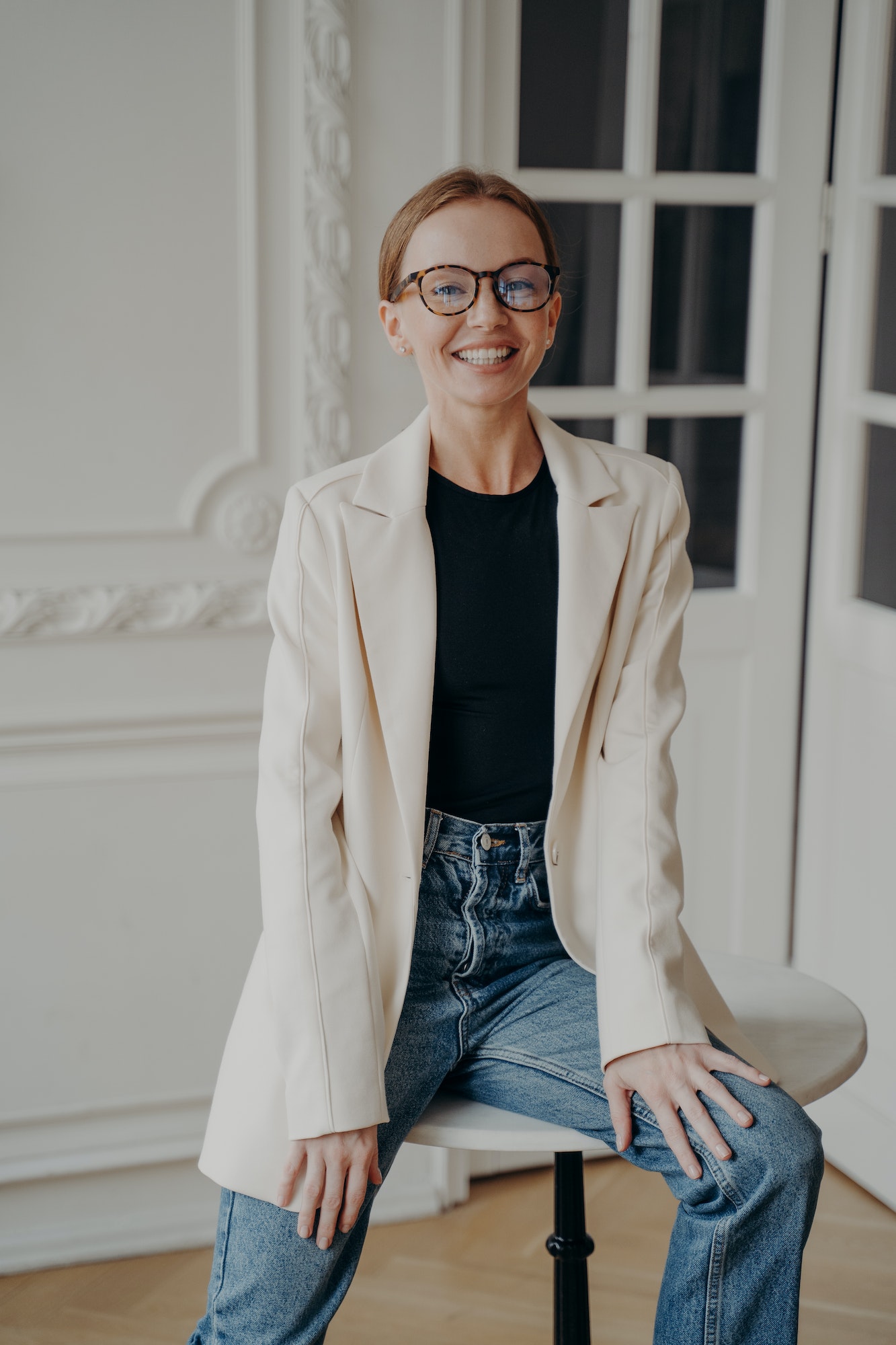 Confident woman sitting on table in apartment. Portrait of gorgeous smiling young adult lady.